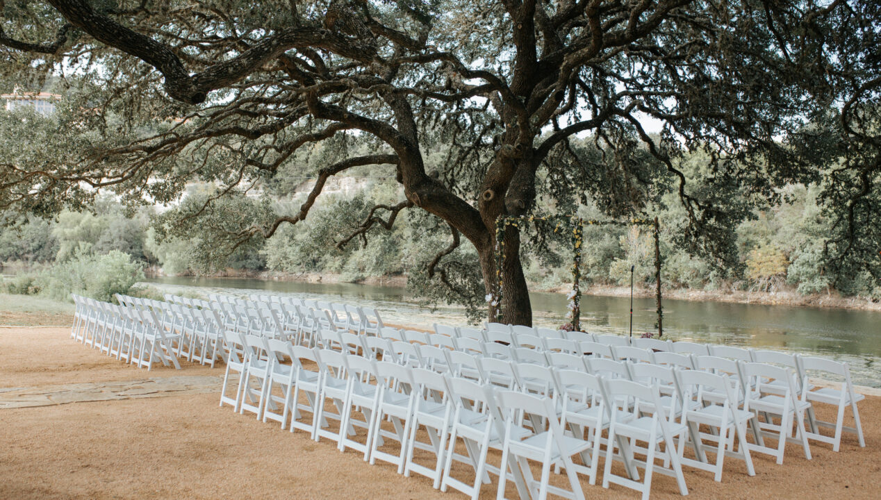 outdoor wedding ceremony setup with white chairs under large tree