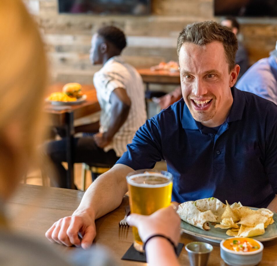 man smiling with beer and chips at table