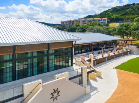 An aerial view of a white building with a metal roof and a large patio with a view of the hills.