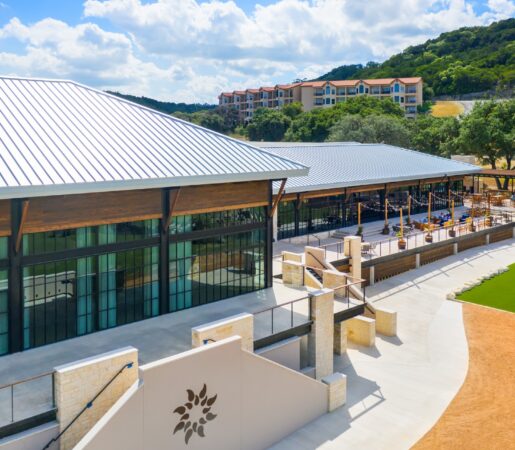 An aerial view of a white building with a metal roof and a large patio with a view of the hills.