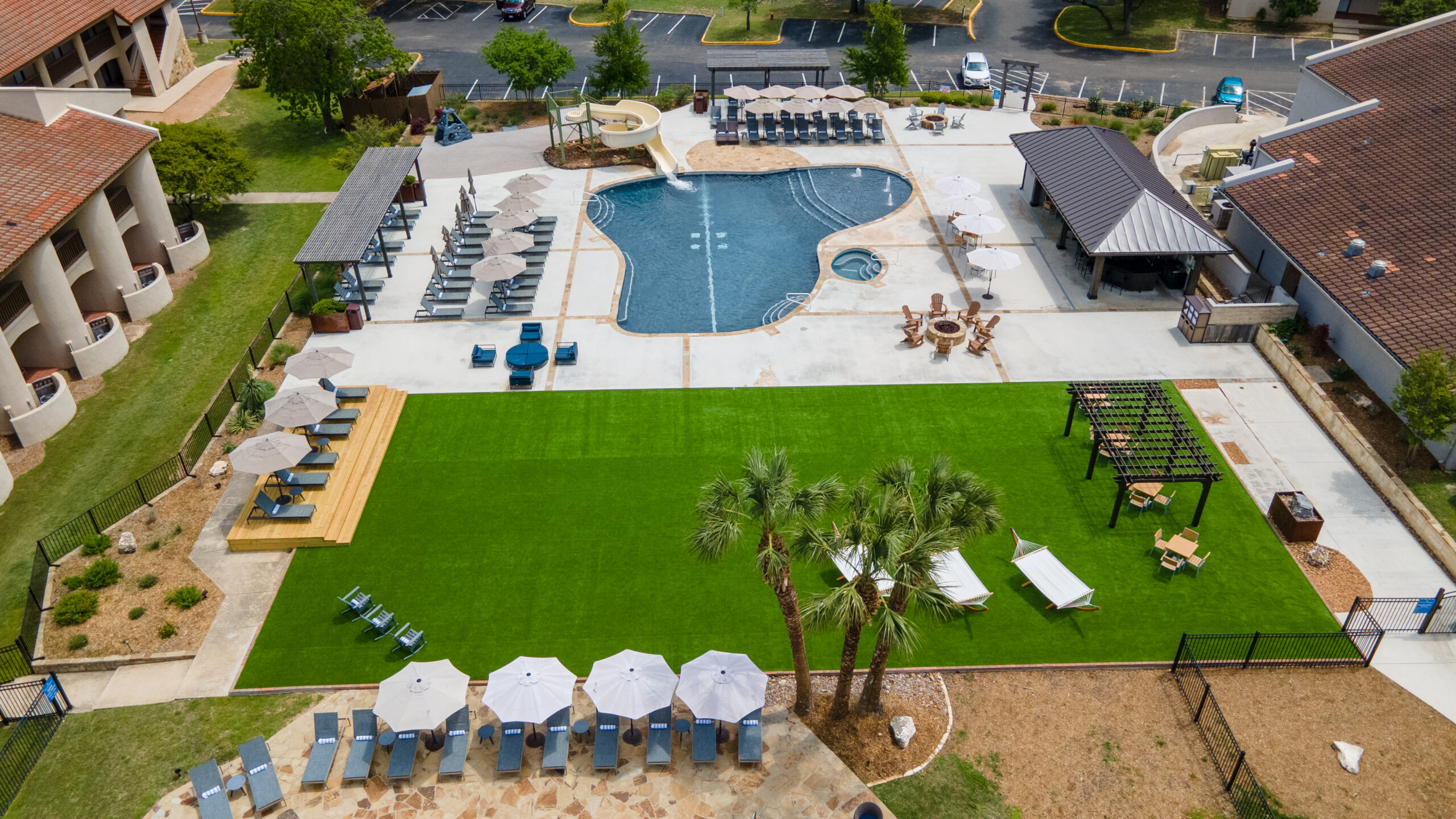 aerial view of resort with swimming pool, lounge chairs, and lawn area with tables and umbrellas