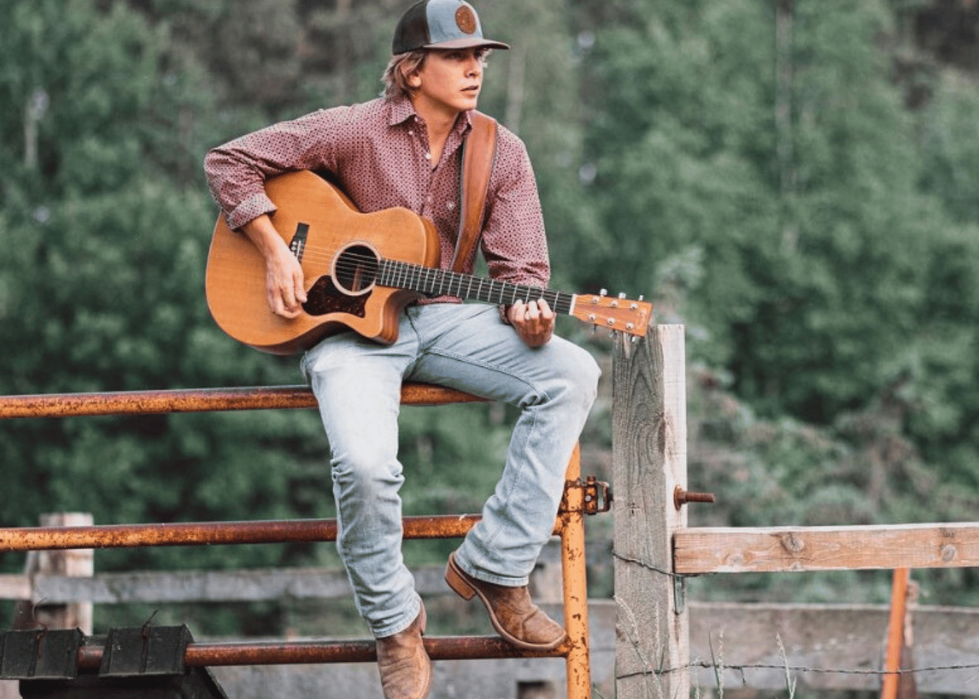 Musician Noah Kurtis with guitar sitting on rustic fence