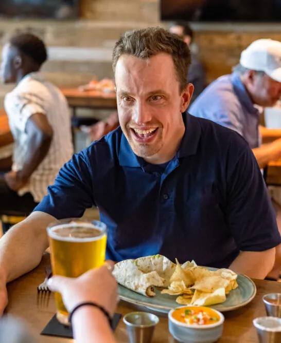 man smiling with beer and chips at table