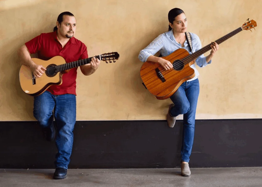 Musicians Jorge and Nicole with guitars leaning on wall
