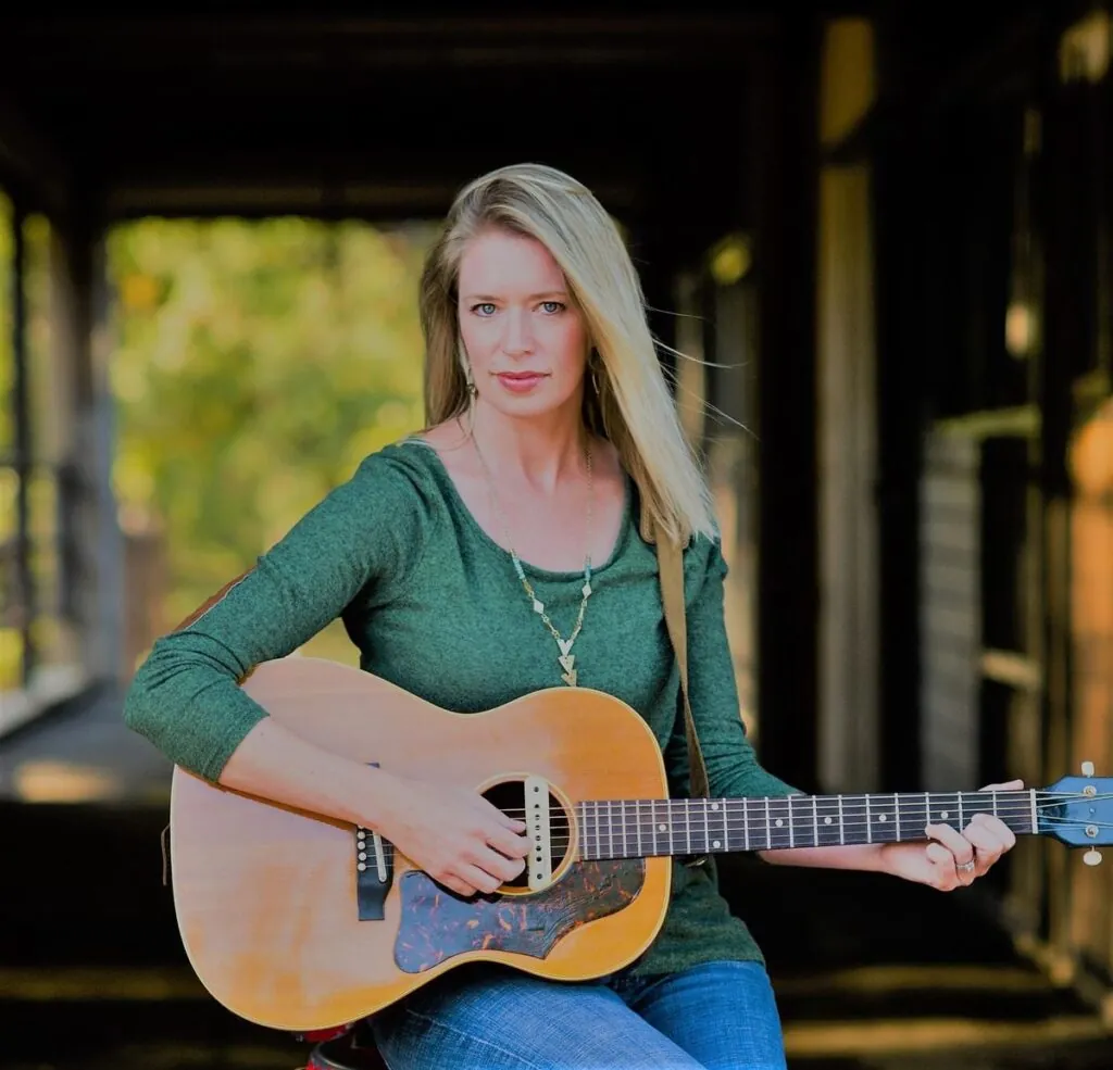 Woman with guitar sitting by barn
