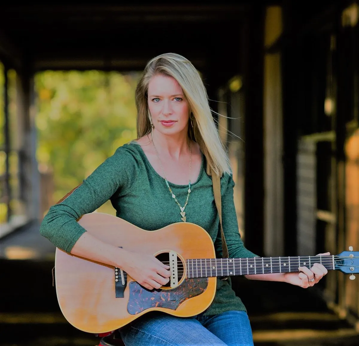 Woman with guitar sitting by barn